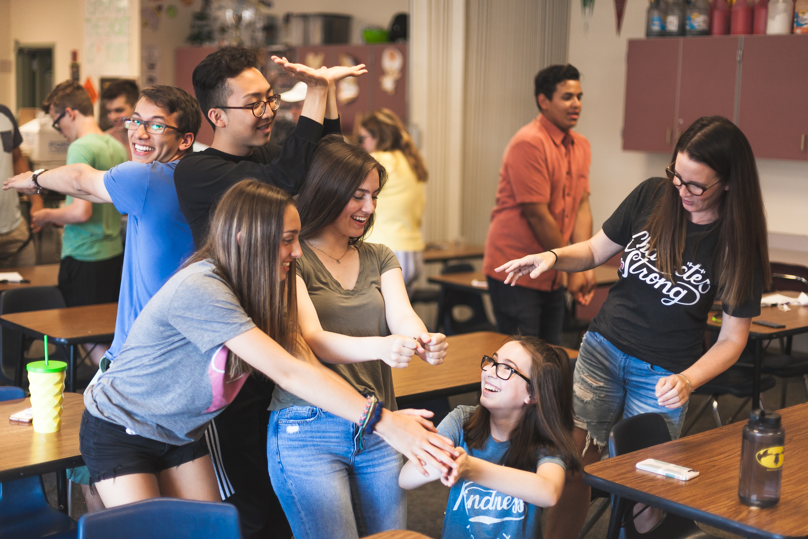 A group of smiling middle school students act out various motions and positions in a group activity