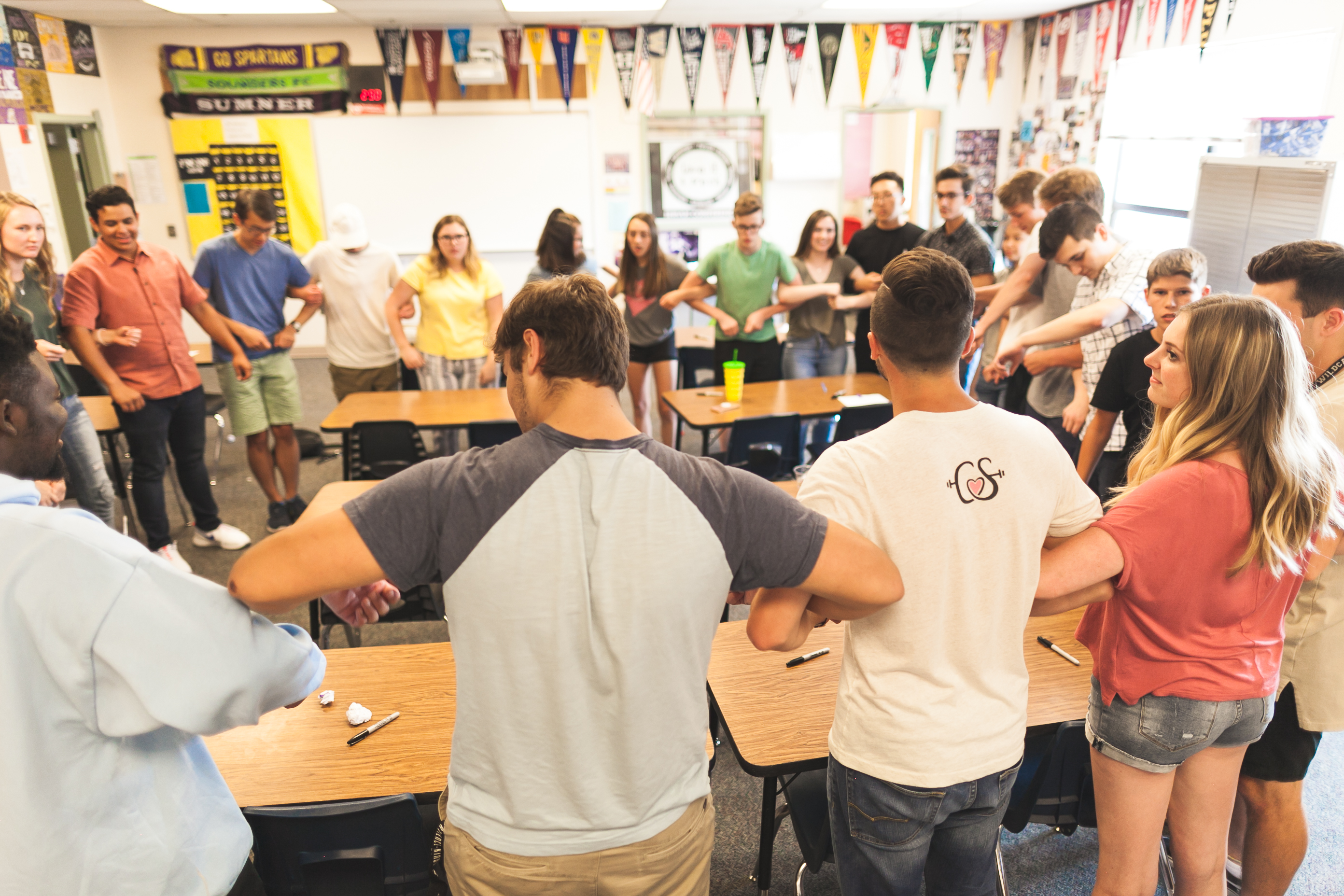 A group of smiling middle school students stand in a circle with their arms linked.